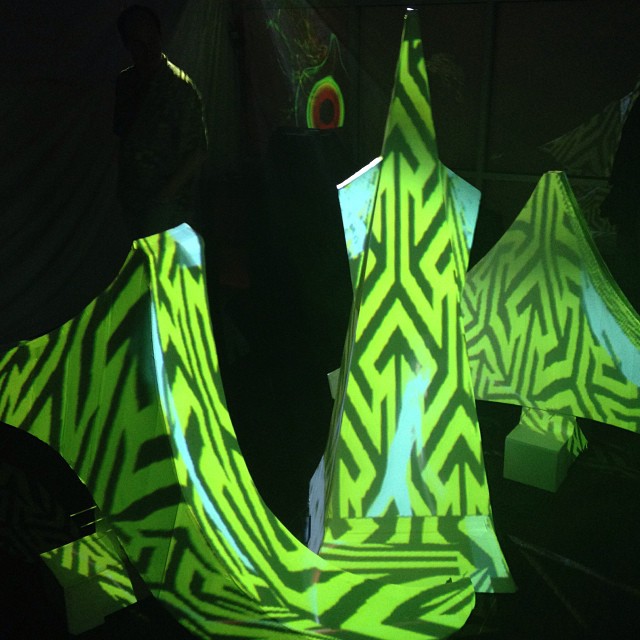 Neon green geometric patterns projection-mapped onto angular 3D sculptural surfaces